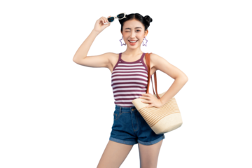 Young Asian woman winking joyfully on summer vacation. She is wearing a striped tank top, denim shorts, and sunglasses, carrying a straw shoulder bag on PNG
