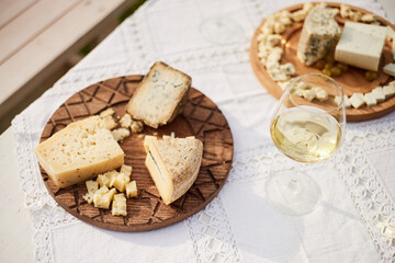 Assorted cheeses arranged on wooden boards with glass of wine placed on embroidered tablecloth, showcasing variety of textures and shapes suitable for gourmet tasting or event
