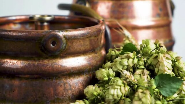 Fresh green hops piled next to a traditional copper brewing kettle for making craft beer.