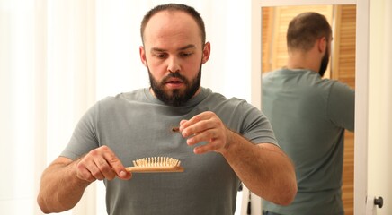 Baldness problem. Worried man taking his lost hair from brush at home