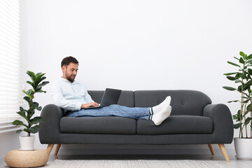 Fototapeta premium Man with laptop on sofa at home. Space for text
