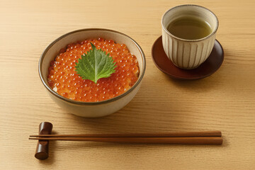 This delicious dish called Ikuradon is presented on a wooden table. The meal includes chopsticks on a rest creating an authentic dining experience.