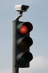 The top light is illuminated red signaling drivers to stop. The cctv camera monitors the intersection for safety and traffic enforcement.