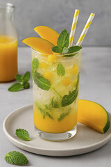 The cold summer cocktail is garnished with fresh mint and mango slices. This delicious tropical drink includes ice and two paper straws.