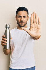 He has a firm expression and is holding a reusable metal water bottle. This could symbolize an anti plastic message or a call to stop.