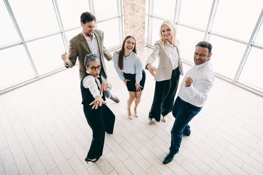 Group of diverse business professionals celebrating and posing energetically in a modern office setting