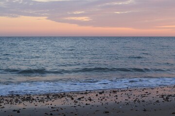Fototapeta premium A seascape at sunset. The pink sky reflects on the wet sand and glare on the water. A play of colors and shades creates a beautiful backdrop. The endless diversity of nature.