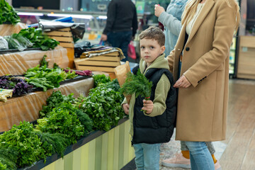A mother and a little boy are standing near the counter at a food market and buying greens for a salad. Healthy nutrition concept. High quality photo