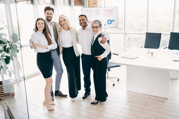 Fototapeta premium Professional team of diverse colleagues in formal attire standing in a modern office environment showcasing teamwork