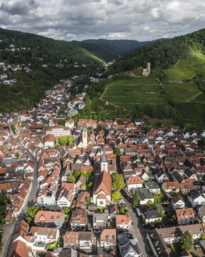 Aerial view of terracotta roofs nestled amongst verdant hills, overlooked by the majestic Strahlenburg Castle ruins, Schriesheim, Baden-Wurttemberg, Germany.