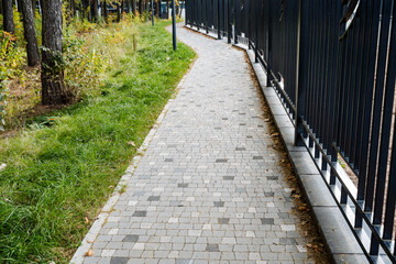 A beautifully curving paved pathway runs through a vibrant landscape, surrounded by lush greenery and a charming fence that enhances the picturesque scenery of this tranquil outdoor space