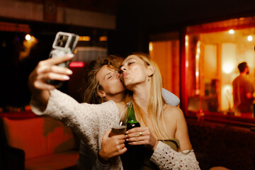 Two happy friends taking a selfie and having fun at a lively party in a cozy indoor setting