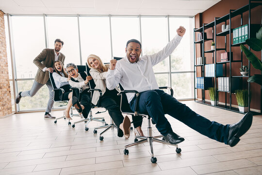 Energetic team having fun racing office chairs in a bright modern workplace, showcasing teamwork