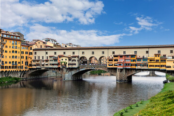 The Ponte Vecchio bridge in Florence showcases its colorful buildings and shops reflecting in the tranquil waters Arno river.