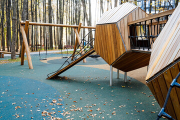 The modern wooden playground structure, beautifully nestled within a serene forest setting, encourages exploration and fun, providing children with an outlet for exercise, imagination, and enjoyment
