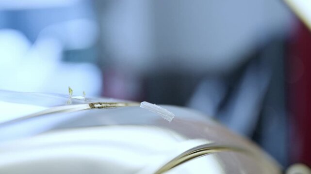 Extreme close-up of a specialized tool being used to remove a small windshield chip or repair minor damage on a car's glossy surface in a professional workshop