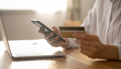 Person using smartphone for online payment while holding credit card laptop in background