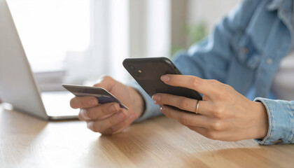 Person using smartphone for online payment while holding credit card laptop in background