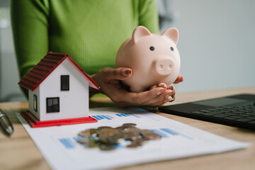 A person saving money with a piggy bank and holding a house model, symbolizing financial planning,...