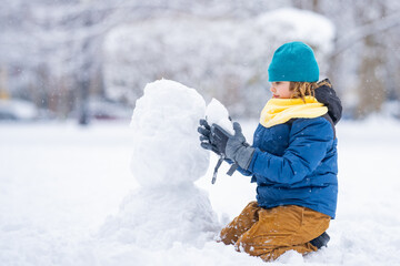Funny Kid make snowballs for snowman in winter. Kid play in snow. Active winter outdoor games. Boy having fun playing with snow. Winter outdoors leisure for kids. Child play on sunny winter day.