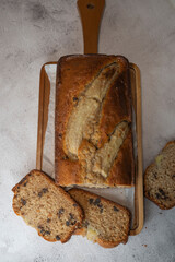 Freshly baked banana bread is sliced and displayed on a wooden cutting board. The bread has a golden-brown crust and chocolate chips, perfect for a cozy snack at home.