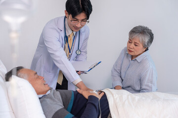 Fototapeta premium scene of a sad senior woman sitting beside elderly man patient who lying on bed getting examine from a doctor