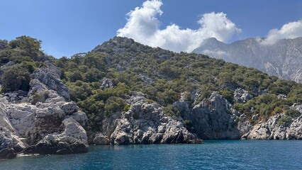 The beautiful rugged coast of Adrasan, Turkey, with green forest and rocky cliffs meeting the calm blue sea. View from a boat on the scenic Turkish Riviera.