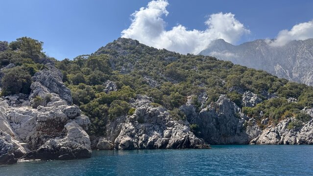 The beautiful rugged coast of Adrasan, Turkey, with green forest and rocky cliffs meeting the calm blue sea. View from a boat on the scenic Turkish Riviera.
