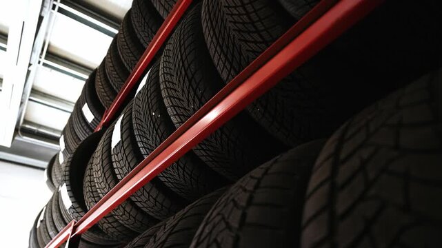 Low angle shot of new winter tires stacked high on red metal shelves in a large automotive garage or warehouse, conveying tire supply and seasonal logistics
