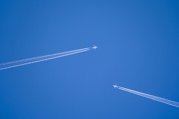 two white jets flying towards each other with long contrails in front of a blue sky	