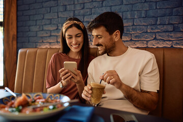 Happy woman and her boyfriends using smart phone in restaurant.
