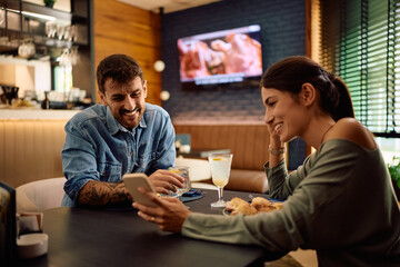 Happy couple using mobile phone during their lunch in restaurant.