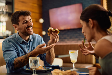 Happy man talking to his girlfriend while eating sandwich in restaurant.