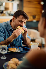 Man with eyes closed enjoying the taste of sandwich in restaurant.