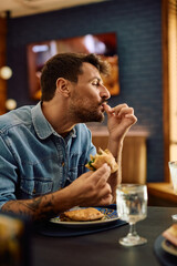 Man with eyes closed enjoying in taste of sandwich in restaurant.