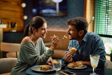 Happy man being feed by his girlfriend while having lunch in restaurant.