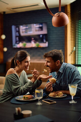 Happy woman feeding by her boyfriend while having lunch in restaurant.