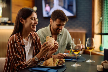 Happy woman enjoying in taste of sandwich during lunch with her boyfriend.