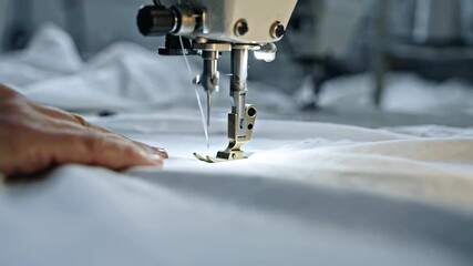 Cinematic video of a textile workshop scene featuring a sewing machine needle stitching a white cotton t-shirt, with ultra-detailed textures, natural lighting, and sharp close-up precision