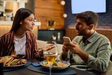 Young couple arguing while using their smart phones during lunch in restaurant.