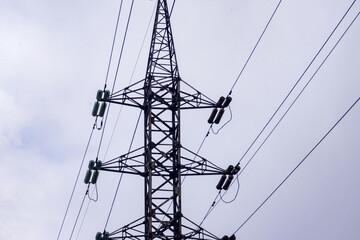 Tall power line tower stands against a cloudy sky transporting electricity across the landscape in...