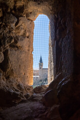 Obraz premium View from the Templar Church tower near Segovia, Spain. The Alcázar is dramatically framed through a dark stone embrasure, contrasting medieval walls and a clear blue sky.