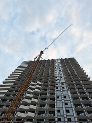 High-rise building under construction with a crane on the side, showing incomplete exterior and open windows, photographed from below