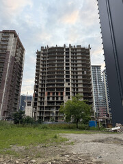 Photo of a multi-storey concrete building under construction, surrounded by other buildings and green foreground