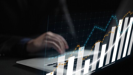 A focused view of hands typing on a laptop, accompanied by digital graphs depicting financial...