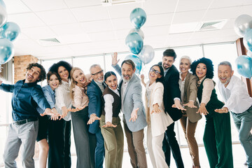 Diverse professional team in formal attire celebrating in an office setting with balloons...