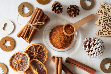 Ground cinnamon and cinnamon sticks with orange slices and pine cones on a white background