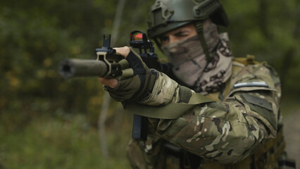 Fototapeta premium Masked army soldier with AR15 carbine. Rifle with a collimator aiming at the camera. Selective focus. Military war recon
