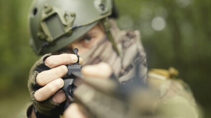 Camouflaged army soldier with AR15 carbine. Rifle with a collimator aiming at the camera. Selective focus. Military recon