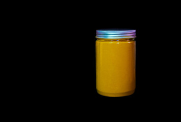 A vibrant yellow turmeric powder fills a clear jar, positioned on a dark black background in a studio setting, showcasing an Indian spice.